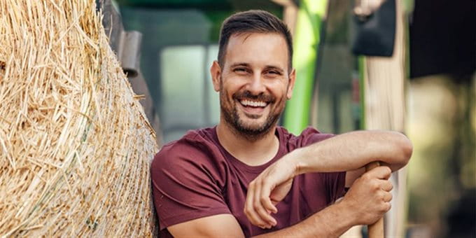 Landwirtschaftler steht an einem Heuballen Landwirtschaftler steht an einem Heuballen