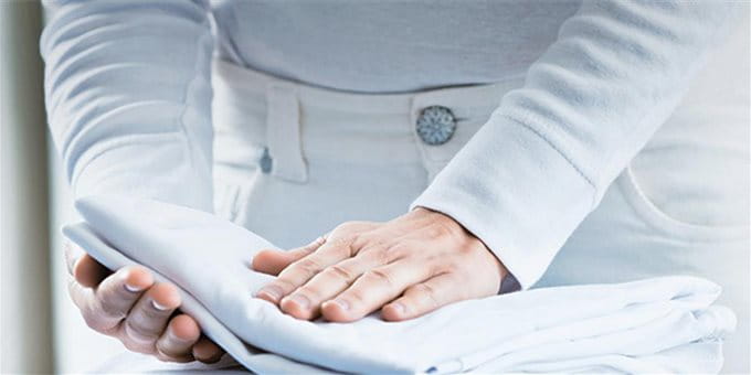 Eine Person faltet Leinentücher auf einem Bügelbrett. Eine Person faltet Leinentücher auf einem Bügelbrett.