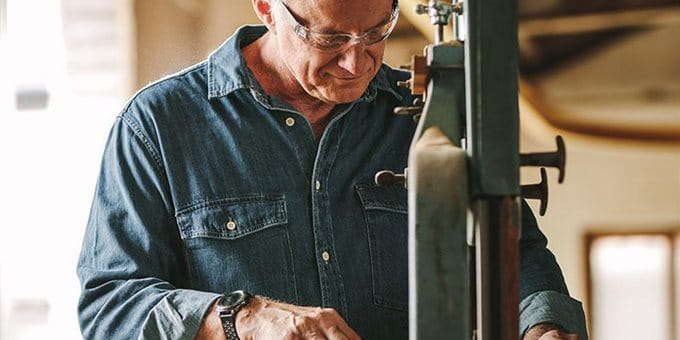 An older man in a blue shirt works on a machine in a workshop. An older man in a blue shirt works on a machine in a workshop.