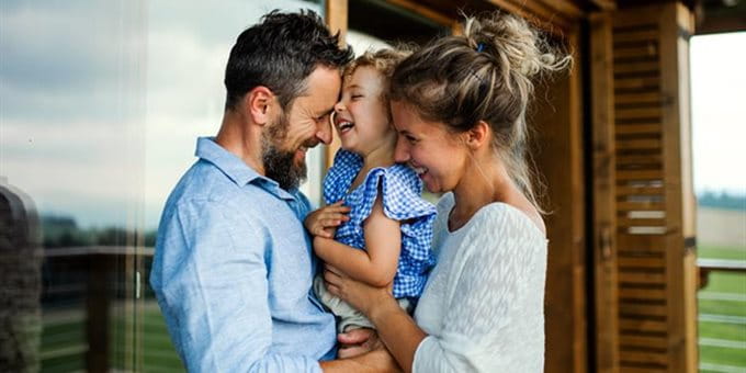 Une jeune famille se tient enlacée sur une terrasse devant une maison et profite d’un moment ensemble en plein air. Une jeune famille se tient enlacée sur une terrasse devant une maison et profite d’un moment ensemble en plein air.