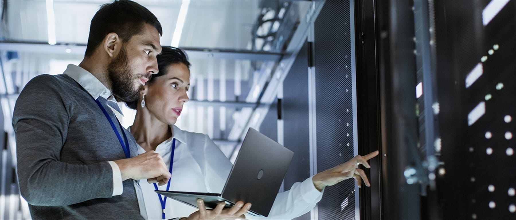 Two IT specialists stand with a laptop in a modern server room and jointly check the server infrastructure. Two IT specialists stand with a laptop in a modern server room and jointly check the server infrastructure.
