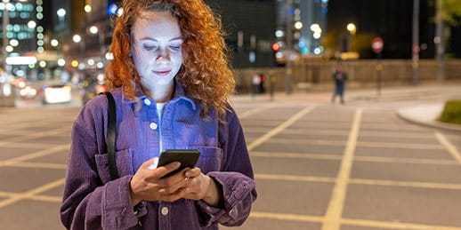Woman stands in a square in the evening and looks at her smartphone Woman stands in a square in the evening and looks at her smartphone