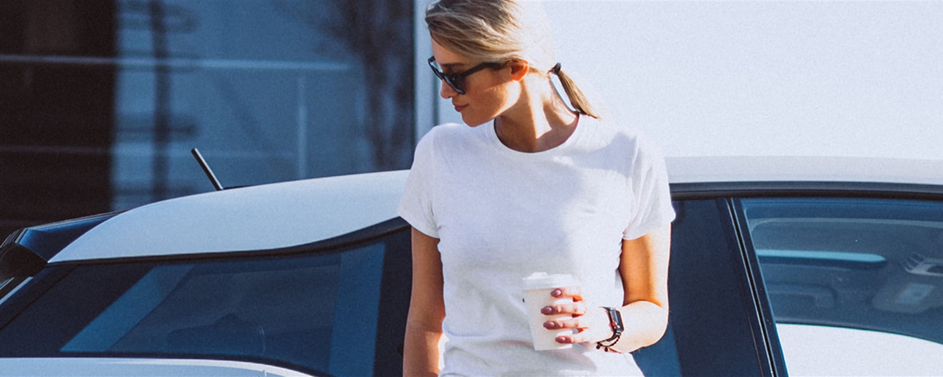 Woman stands in front of her car at the electric charging station and drinks coffee Woman stands in front of her car at the electric charging station and drinks coffee