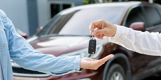 A person hands over car keys to another person in front of a parked car A person hands over car keys to another person in front of a parked car