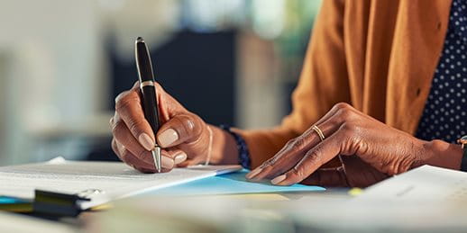 A close-up of a person's hand writing with a pen on a piece of paper, surrounded by documents and stationery. A close-up of a person's hand writing with a pen on a piece of paper, surrounded by documents and stationery.