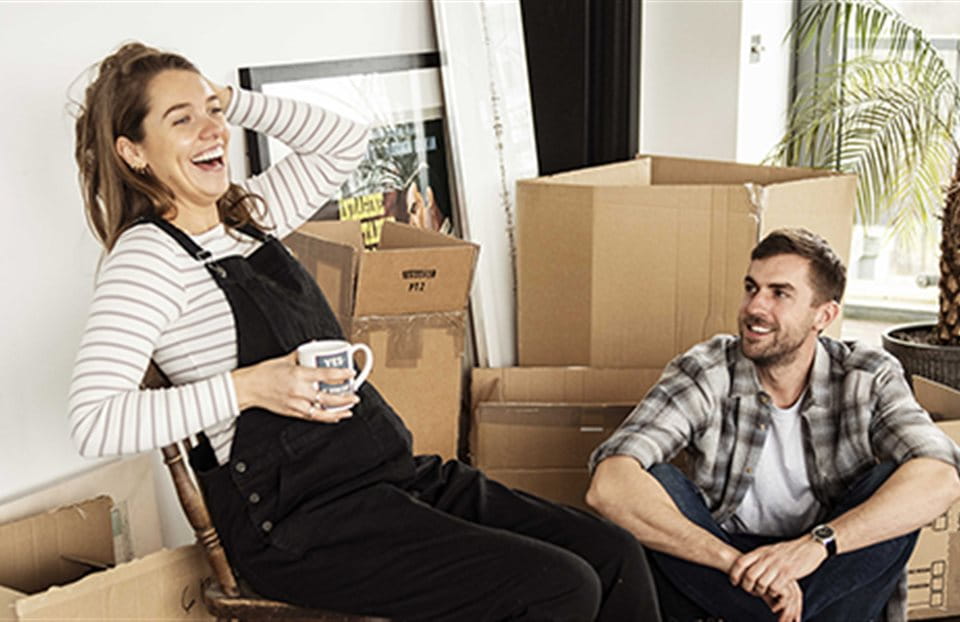 A couple is sitting between moving boxes and laughing. A couple is sitting between moving boxes and laughing.