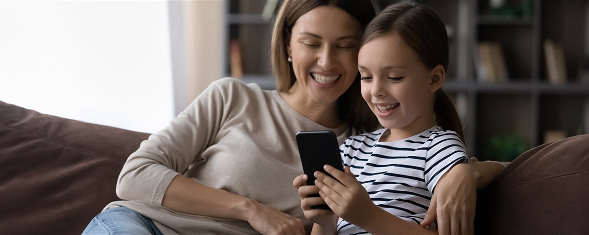 Mother sits with her daughter on the sofa and looks at a smartphone. Mother sits with her daughter on the sofa and looks at a smartphone.