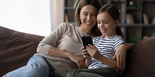 Mother sits with her daughter on the sofa and looks at a smartphone. Mother sits with her daughter on the sofa and looks at a smartphone.