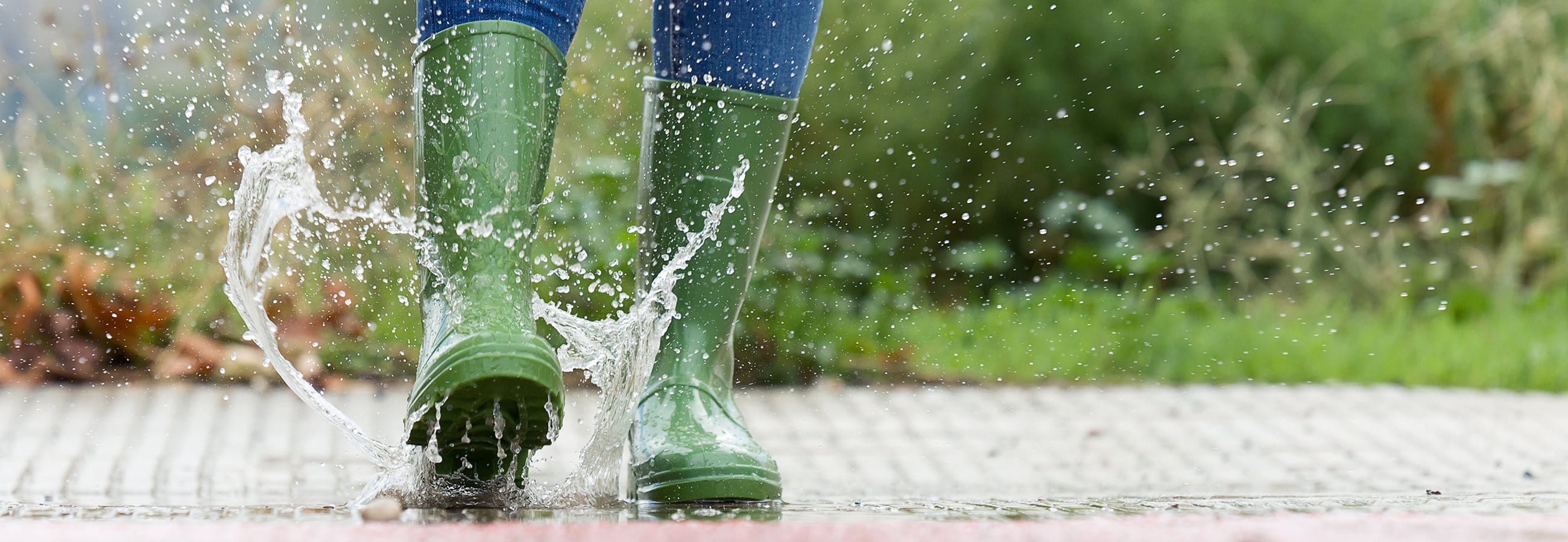 Woman jumps into puddle in green wellies Woman jumps into puddle in green wellies