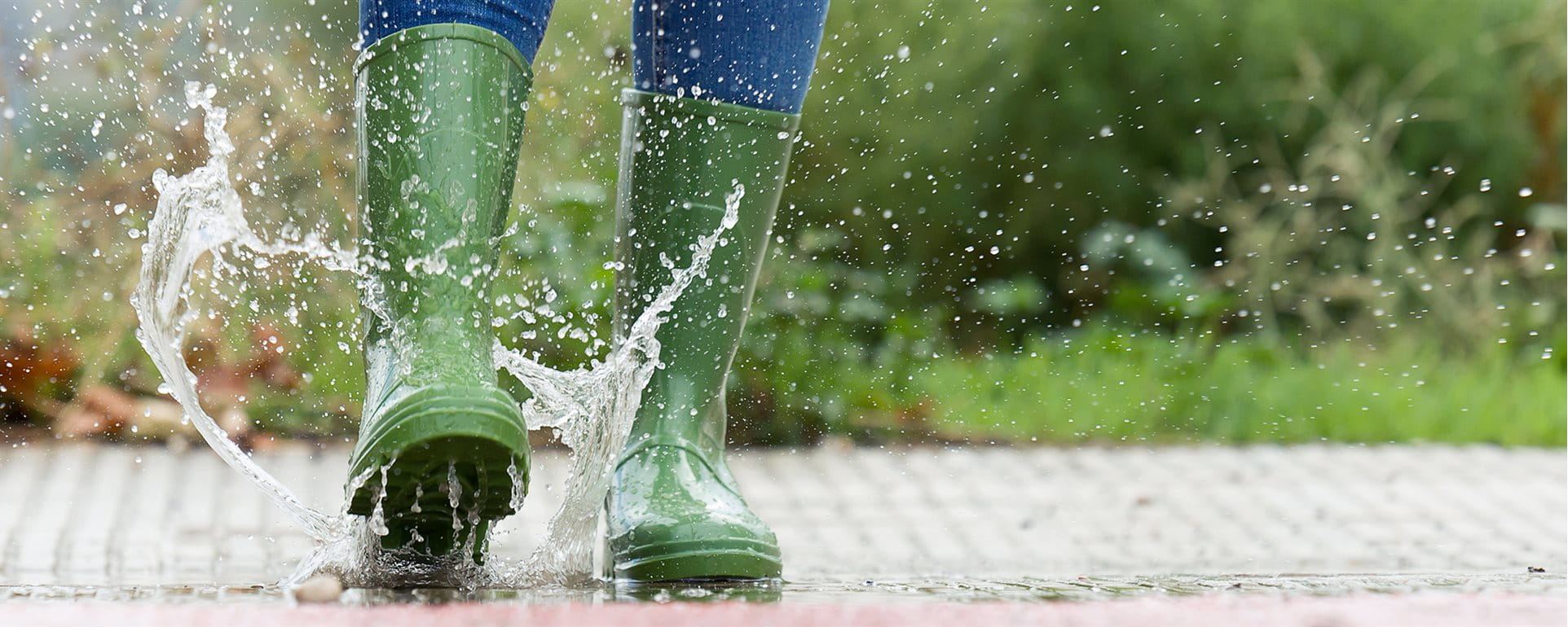 Woman jumps into puddle in green wellies Woman jumps into puddle in green wellies