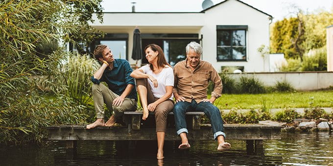 Trois personnes assises ensemble sur un ponton devant une maison au bord de l’eau. Trois personnes assises ensemble sur un ponton devant une maison au bord de l’eau.